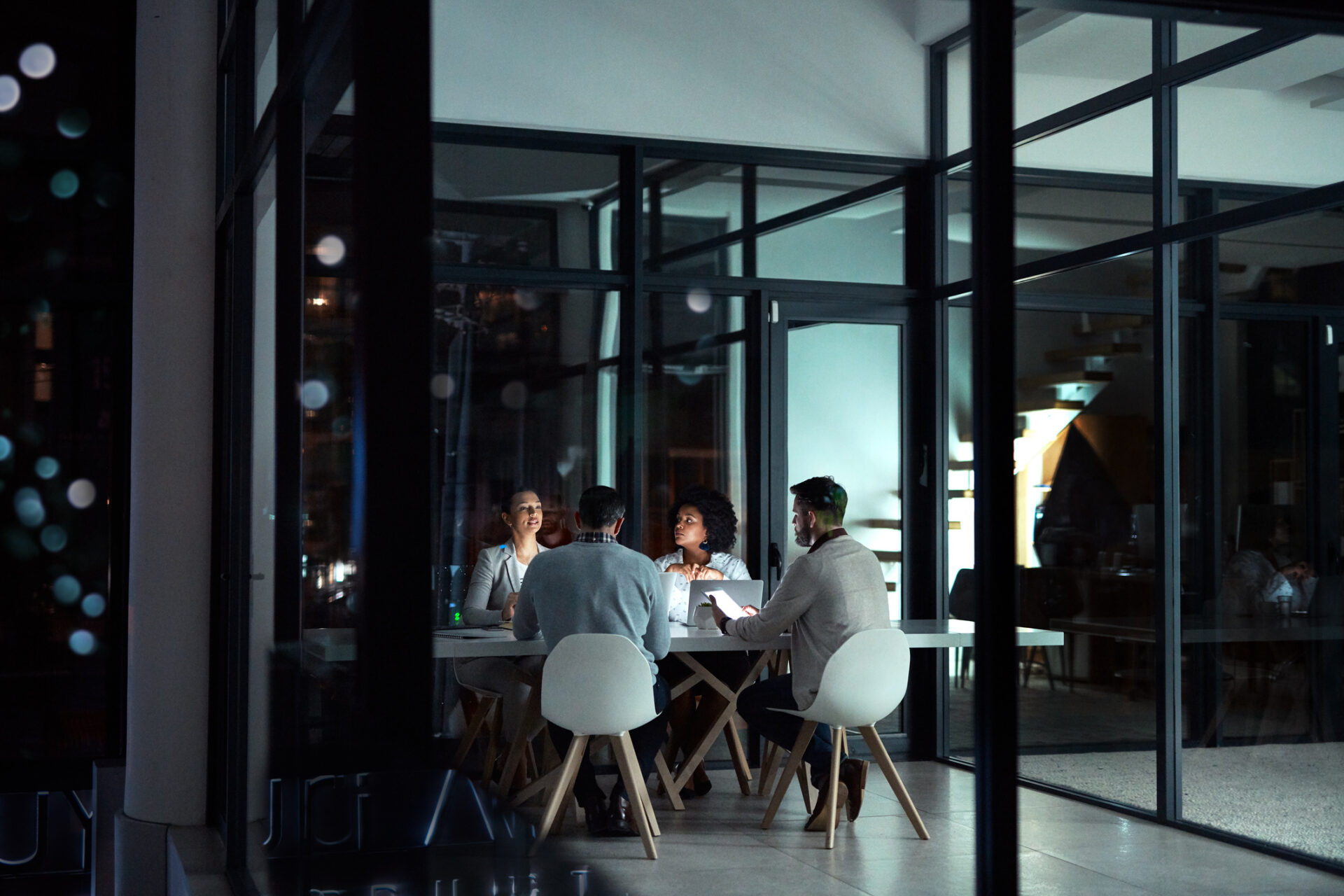 Diverse business team collaborating in a glass-walled conference room during an agency evaluation meeting.